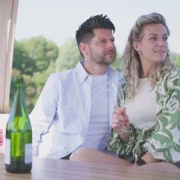 Koppel geniet op een luxe jacht van he uitzicht terwijl de open fles wijn op een tafeltje voor hen staat.