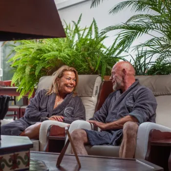 Twee personen ontspannen in badjas bij Top Alivio, zittend in een rustige, groene wellnessomgeving.